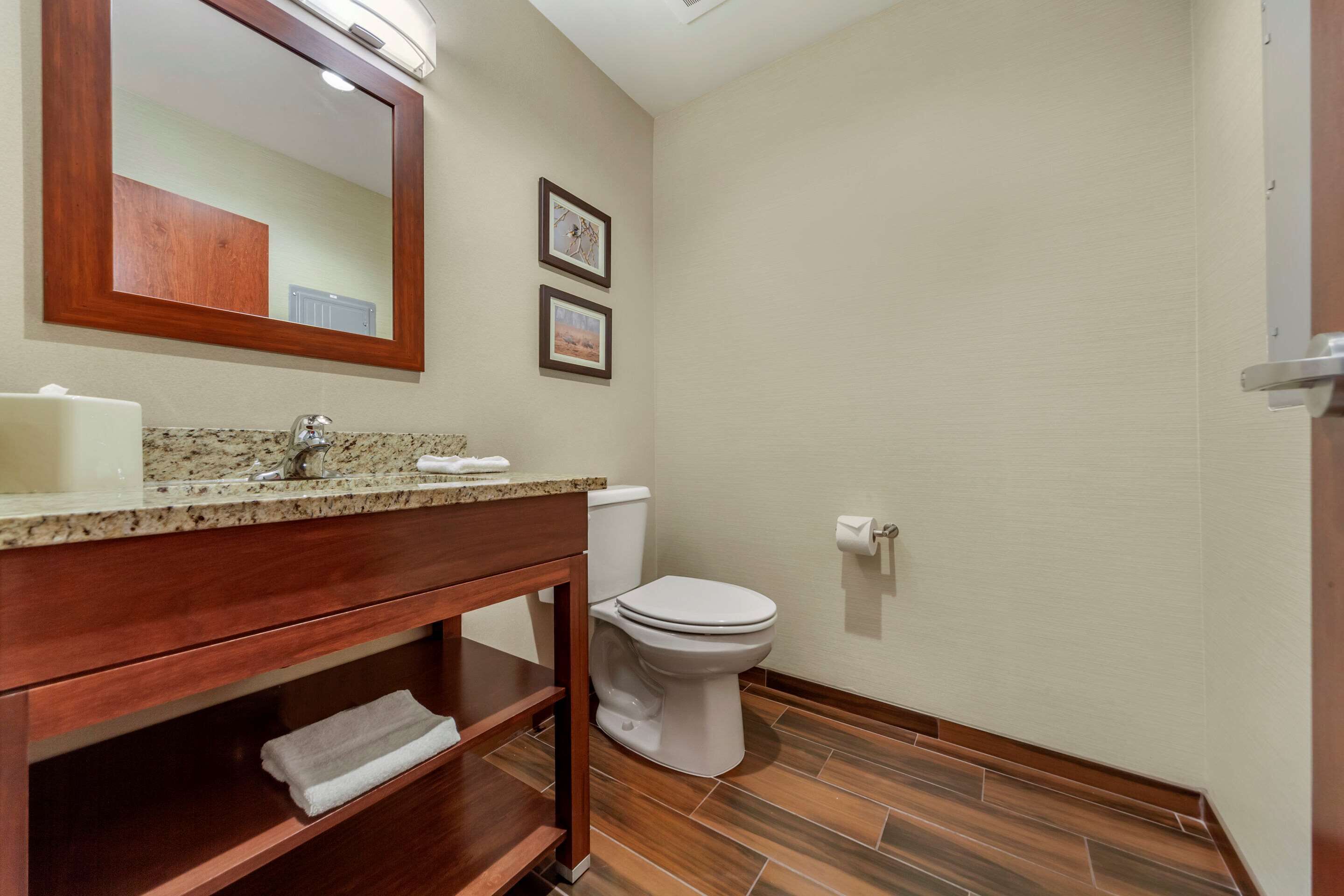 A bathroom with a wooden vanity, a sink, a toilet, and framed pictures on the wall.