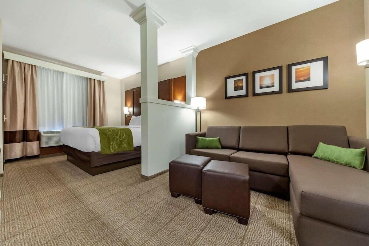 Ett hotellrum med en säng, en soffa, en pall, en lampa och inramade tavlor på väggen.