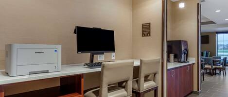 A reception area with a Samsung printer, a computer, and a flat-screen TV on a counter. There are two beige chairs and a coffee machine.