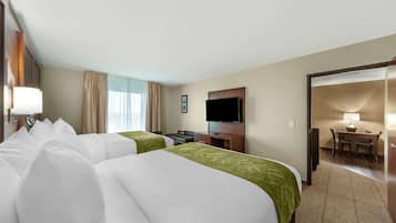 A hotel room with two beds, a desk, a television, and a dining area.
