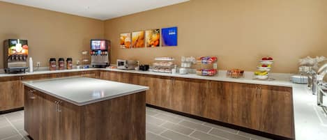 A modern hotel lobby with a central island, a coffee station, and a fruit display.