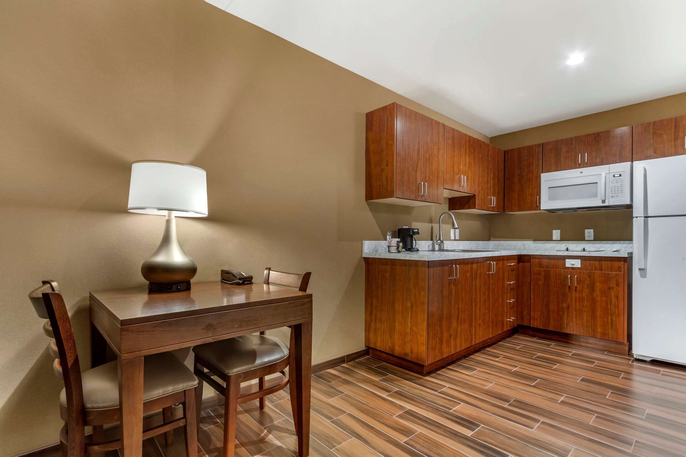 A compact kitchen with wooden cabinets, a microwave, a refrigerator, and a dining table with chairs.