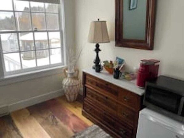 A room with a wooden dresser, a lamp, a vase, and a window with a view of buildings.