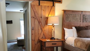Un dormitorio con una cama de madera, una mesita de noche con lámpara y una rústica puerta de granero.