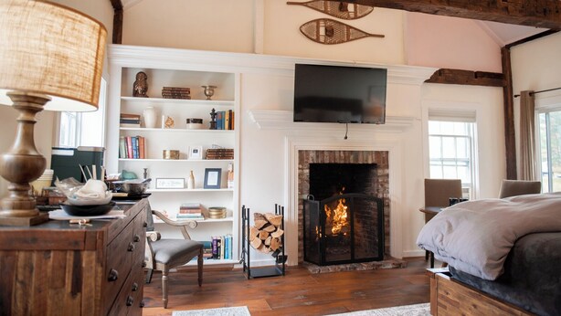 Una habitación acogedora con chimenea, vigas de madera, una estantería y un televisor.