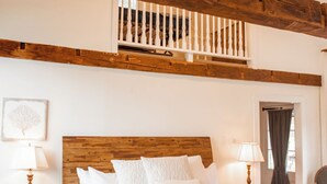 Un dormitorio con cabecera de madera, cama con ropa blanca, almohada 'RELAX', mesita de noche con lámpara y vistas al balcón.