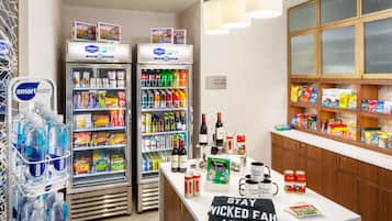 Zona de recepción de hotel con dos refrigeradores llenos de bebidas, aperitivos y una máquina de café. Se indica la disponibilidad de una tienda de suites.