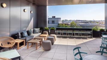 A rooftop terrace with a sofa, chairs, tables, and potted plants.