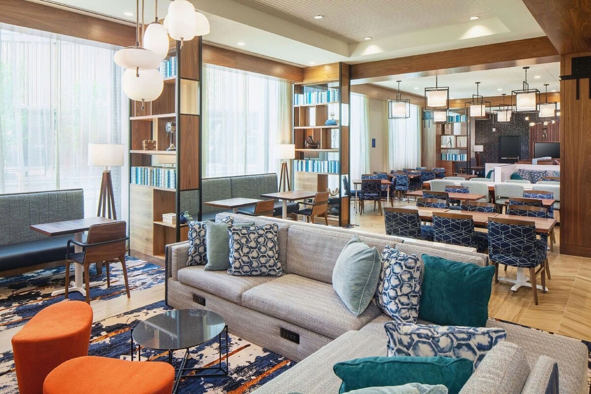 A modern hotel lobby with a sofa, chairs, tables, and a TV.