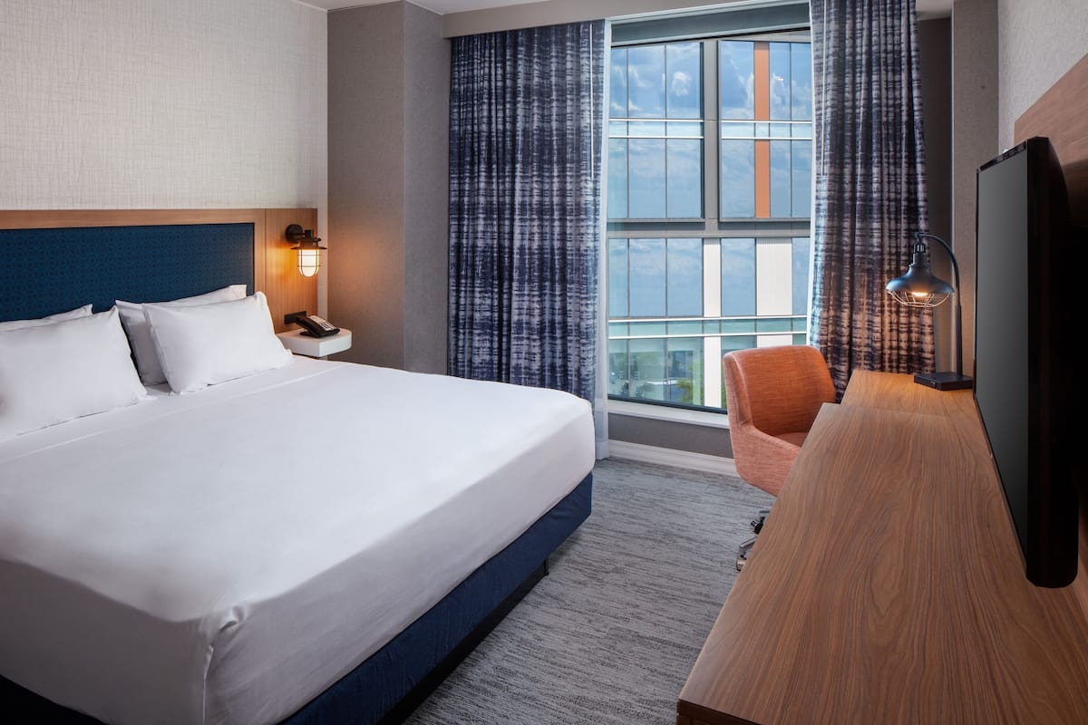 A hotel room with a large bed, a desk, a chair, a TV, and a window with curtains.