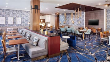 Un vestíbulo de hotel con área de bar, asientos y una pantalla grande.