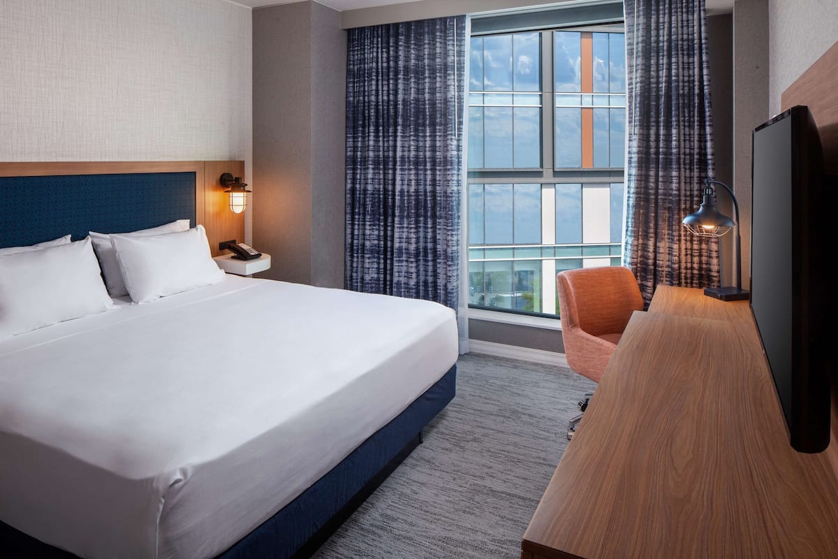 A hotel room with a large bed, a desk, a chair, a TV, and a window with curtains.