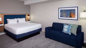 Una habitación de hotel con una cama grande, un sofá azul, un cuadro enmarcado en la pared y una mesita de noche con una lámpara.