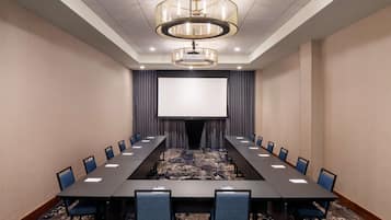 A conference room with a long table, chairs, a projector screen, and a carpeted floor.