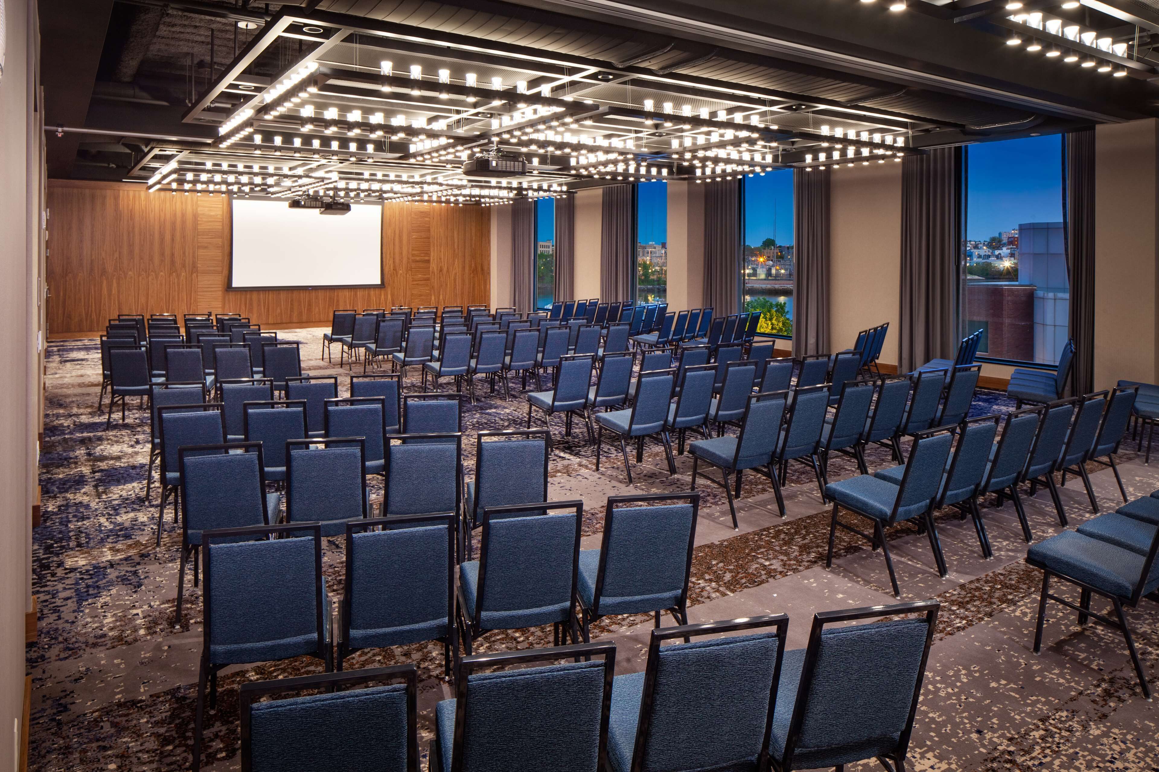 A conference room with rows of chairs, a large screen, and a city view.