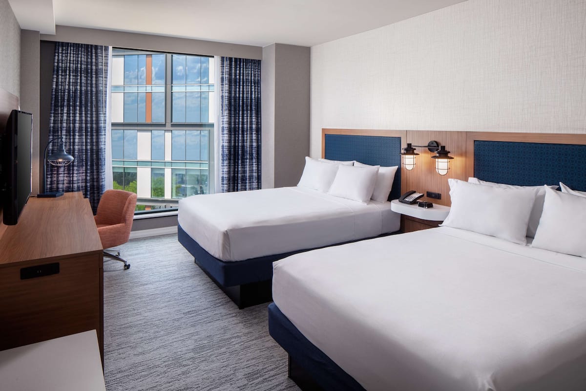 A hotel room with two beds, a desk, a chair, a TV, and a window with curtains.