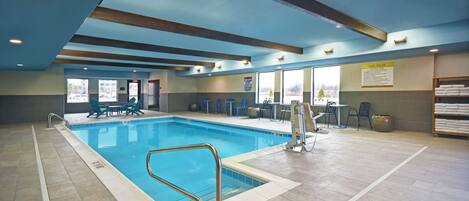 An indoor swimming pool with clear lanes, a changing room area, and a seating area with tables and chairs.