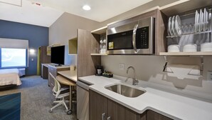 A compact hotel room with a kitchenette, a bed, a desk, and a window with a view. - Home2 Suites by Hilton Springdale Cincinnati (Cincinnati)
