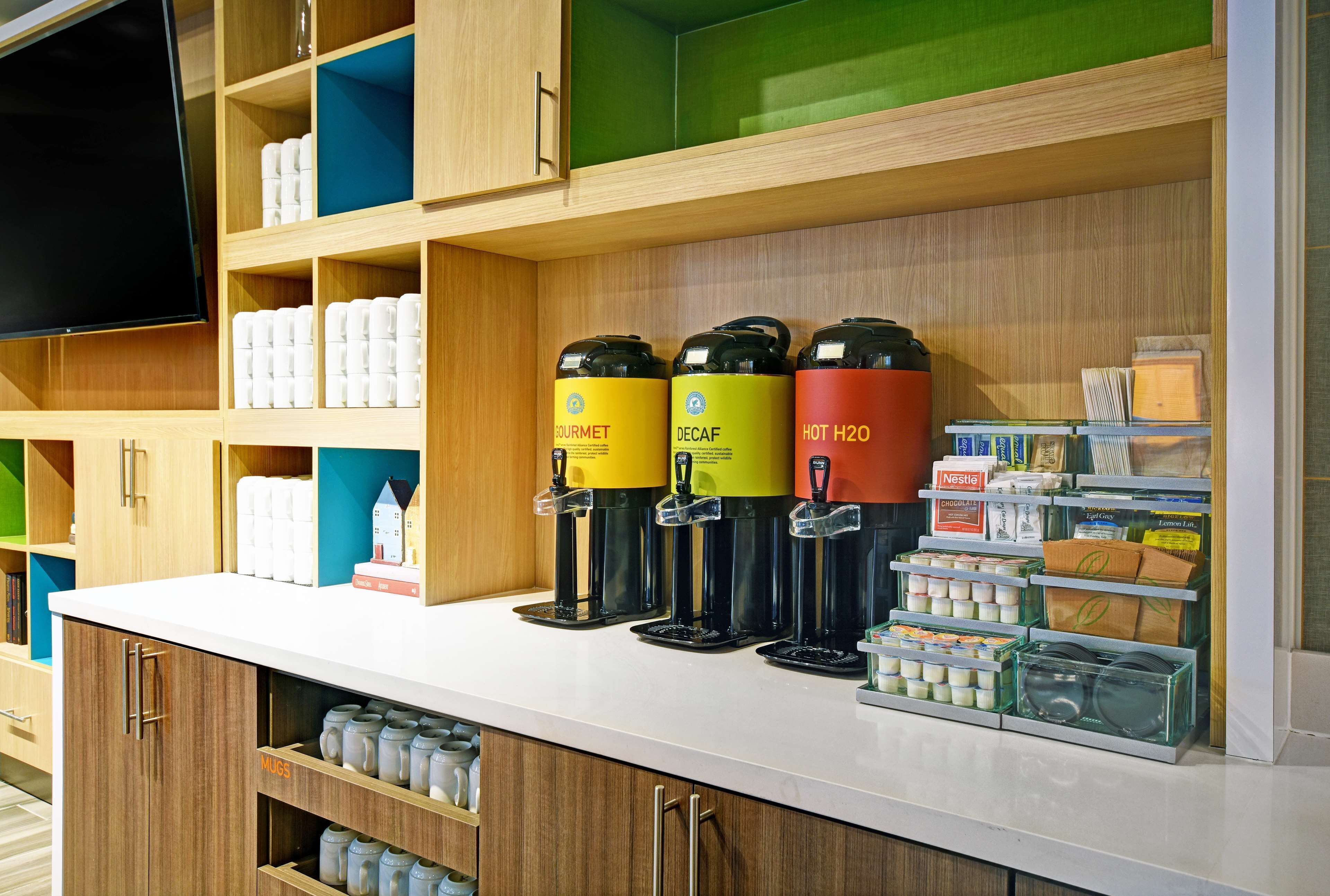 A kitchen area with a white countertop, wooden cabinets, and a shelf with various kitchen appliances and containers.