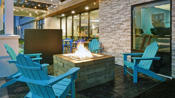 An outdoor seating area with a fire pit and Adirondack chairs. - Home2 Suites by Hilton Springdale Cincinnati (Cincinnati)