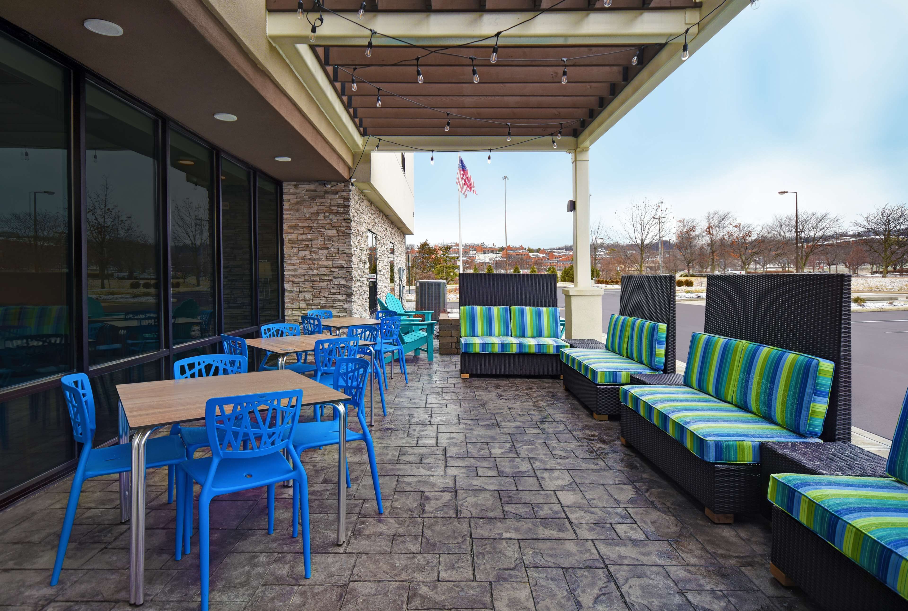 Eine Terrasse im Freien mit blauen Stühlen und Tischen, einer Steinsäule und einem überdachten Sitzbereich mit gestreiften Kissen.