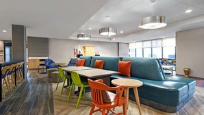 A modern dining area with a long table, colorful chairs, a blue sofa, and a small round table. - Home2 Suites by Hilton Springdale Cincinnati (Cincinnati)