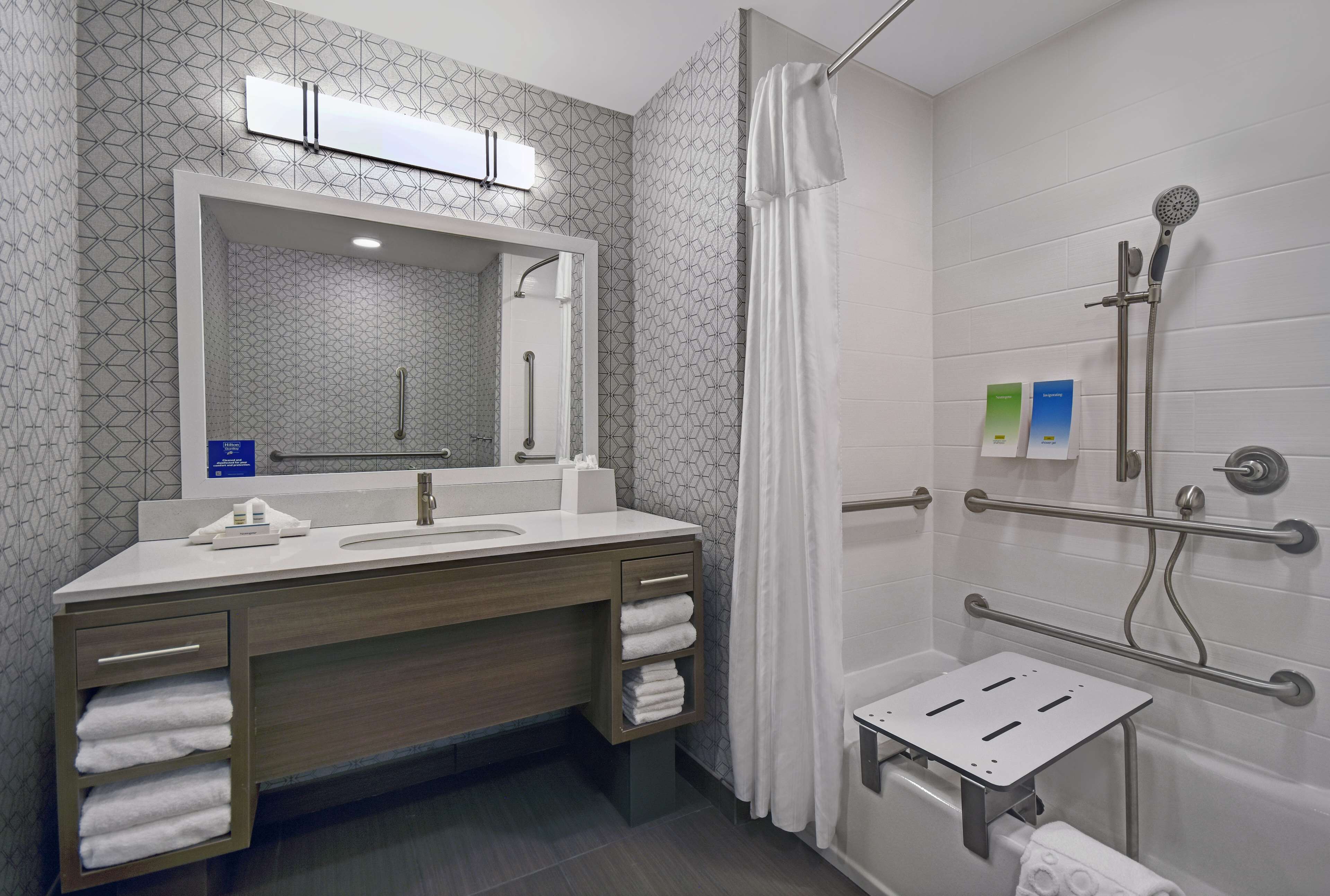 Un baño moderno con un espejo grande, lavamanos dobles, ducha con cabezal de ducha de mano y barra de apoyo.