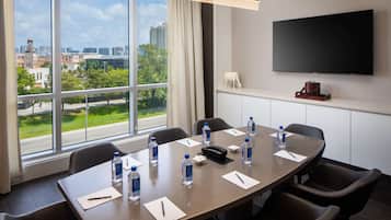 A conference room with a large table, chairs, a TV, and a view of a cityscape through large windows.