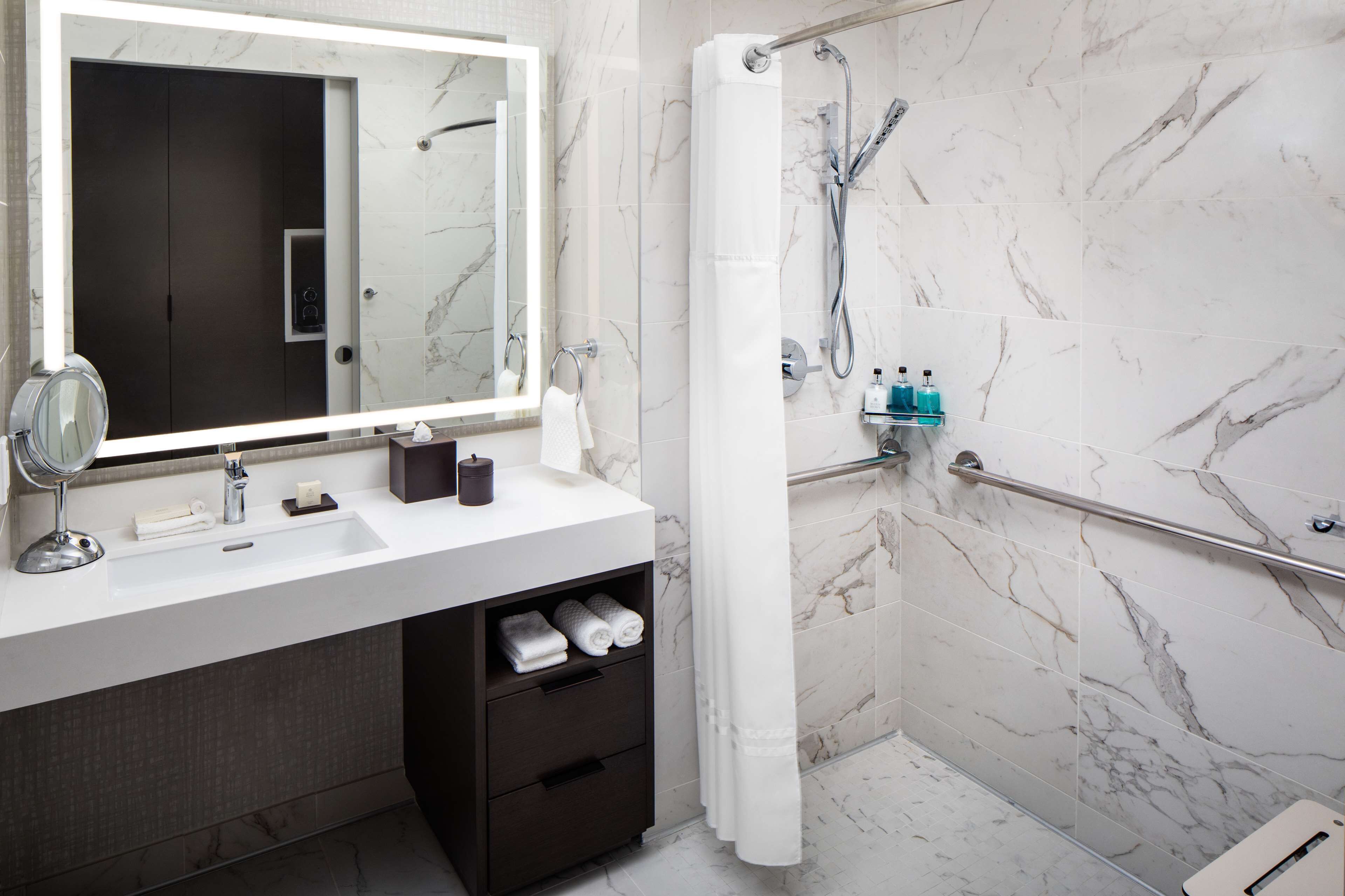 A modern bathroom with a marble-tiled shower, a white sink with a mirror, and a towel rack.