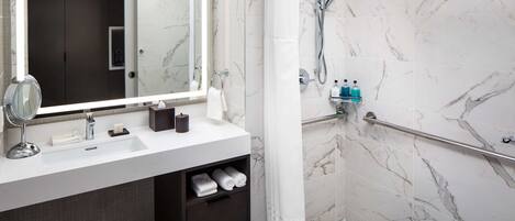 A modern bathroom with a marble-tiled shower, a white sink with a mirror, and a towel rack.