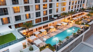 Un hotel moderno con piscina en la azotea, varios balcones y mobiliario exterior.