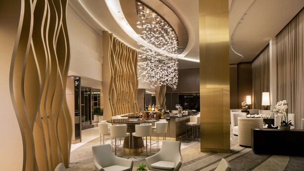Un moderno vestíbulo de hotel con una zona de bar, espacios de descanso e iluminación decorativa.