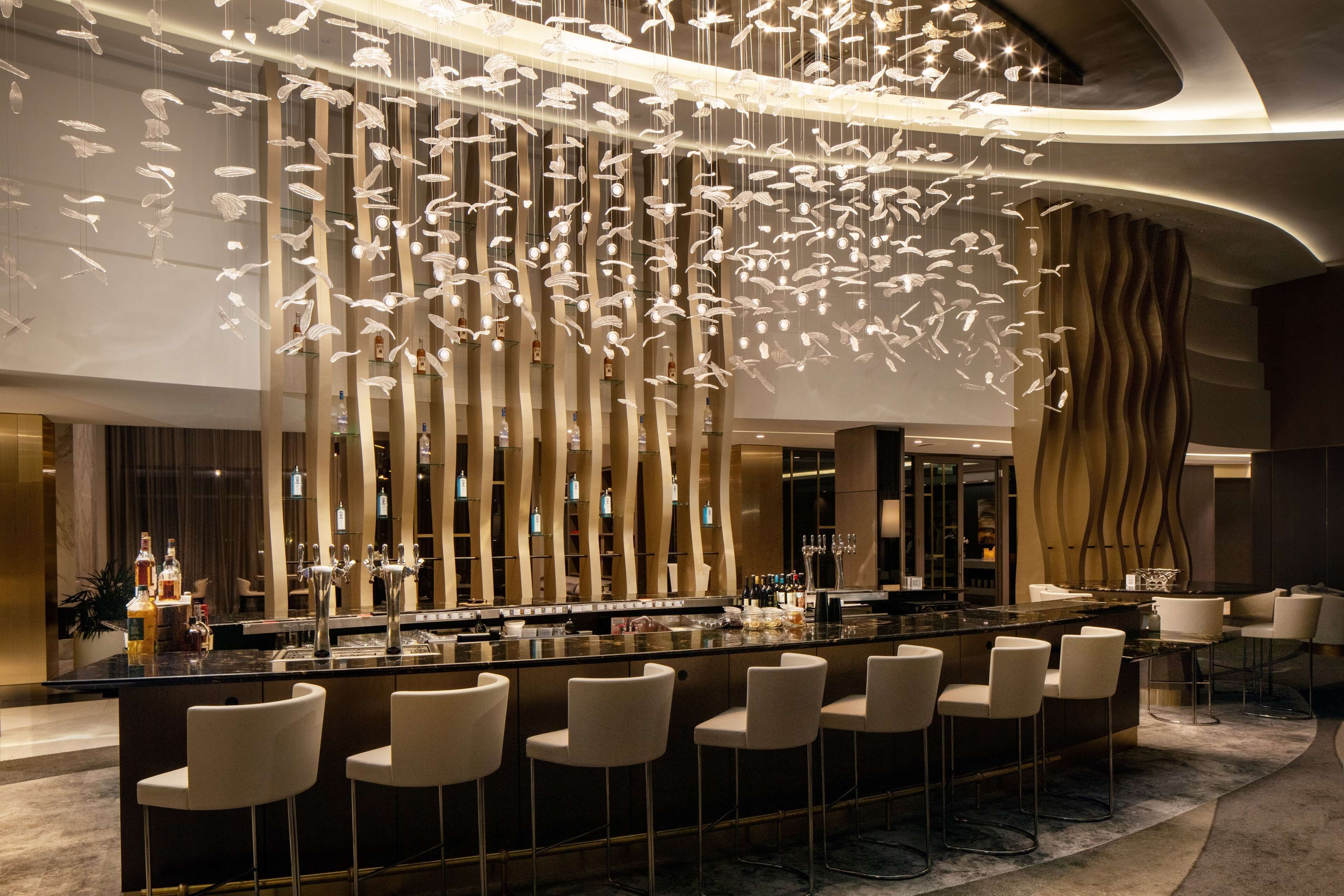 A modern bar area with a central island, bar stools, and a unique ceiling light installation.