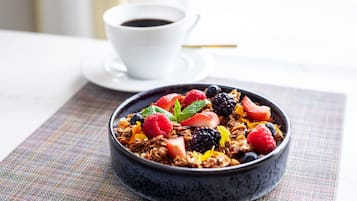 A bowl of granola with mixed berries and mint leaves, accompanied by a white cup of coffee on a table.