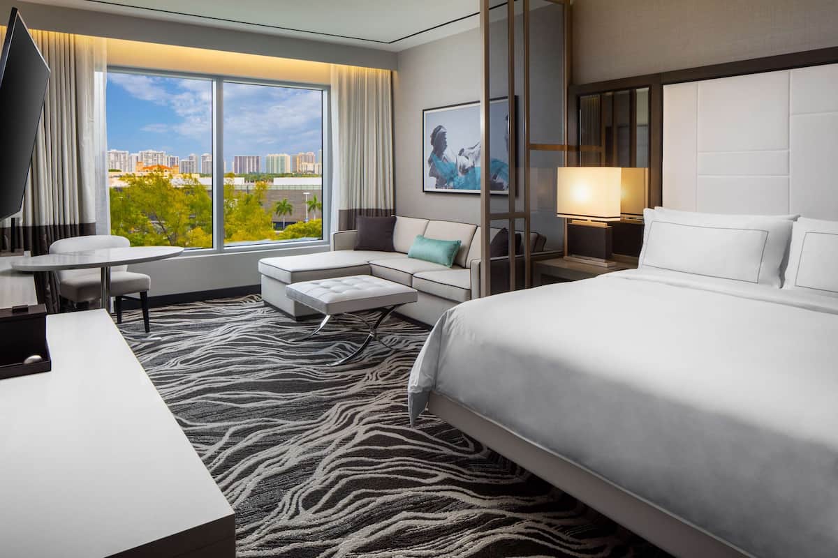 A modern hotel room with a large bed, a desk, a sofa, and a view of the cityscape.