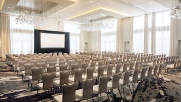Un salón de conferencias con filas de sillas, una pantalla grande y candelabros.