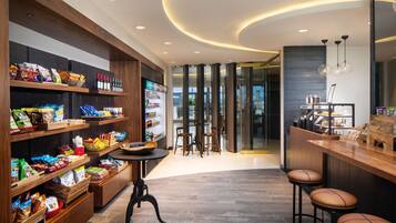 A modern interior with wooden shelves stocked with snacks and beverages, a bar area with stools, and a seating arrangement with tables and chairs.