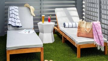 Two lounge chairs with cushions, a small table with drinks, and a straw hat on the table.
