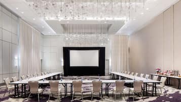 A conference room with a long table, chairs, a large screen, and a chandelier.