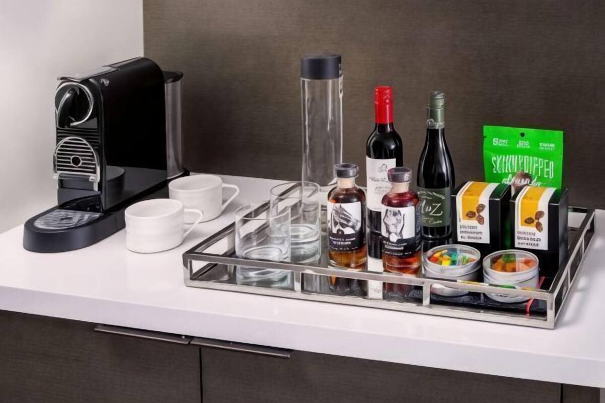 A breakfast tray with a coffee maker, wine bottles, and food containers on a hotel counter.