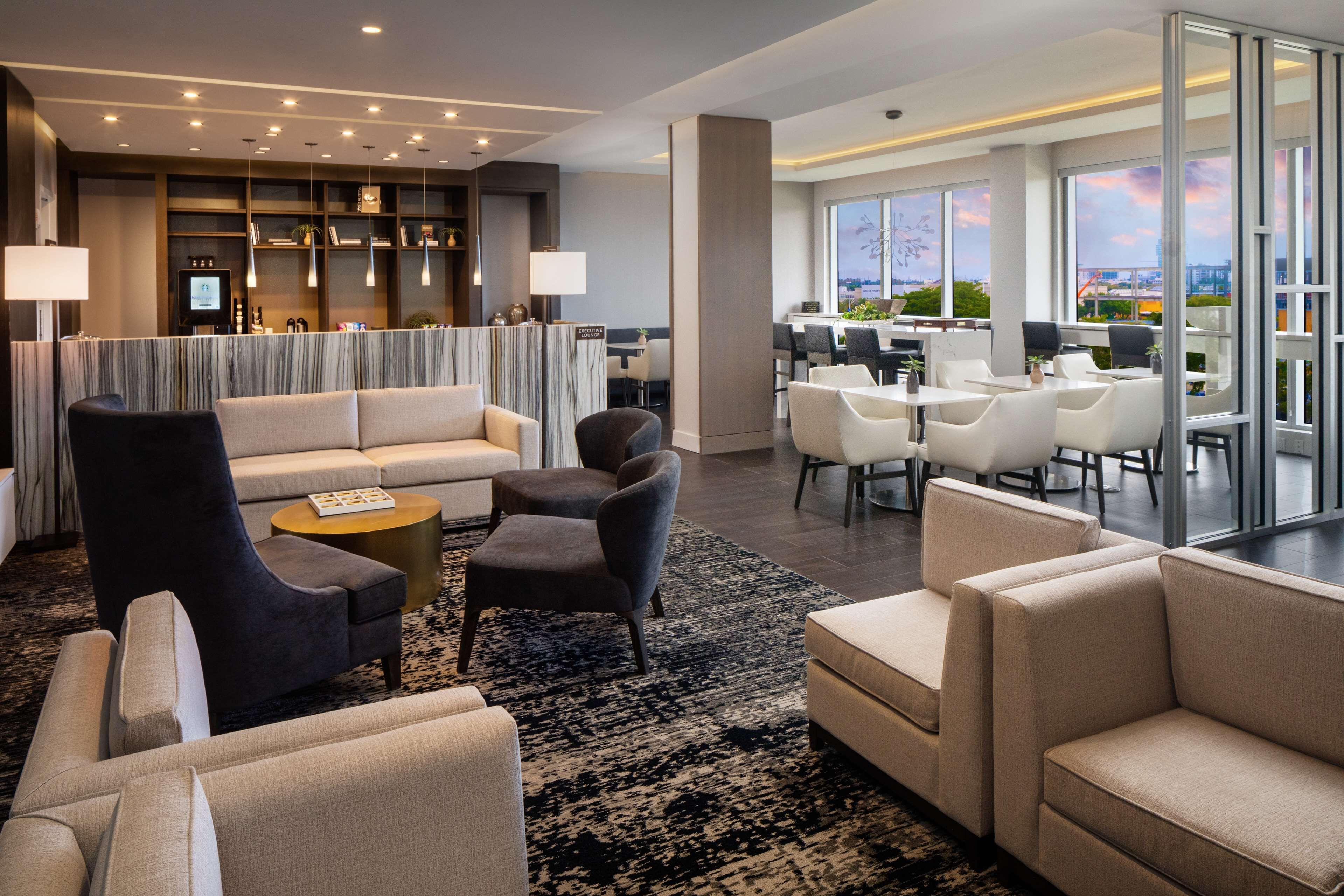 Un hall d’hôtel moderne avec un canapé, des fauteuils, une table basse et un espace repas comprenant des tables et des chaises.