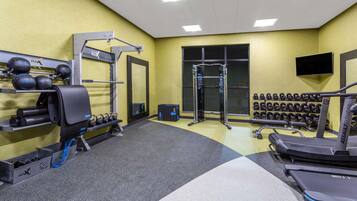 A gym with weightlifting equipment, treadmills, and a TV mounted on the wall.