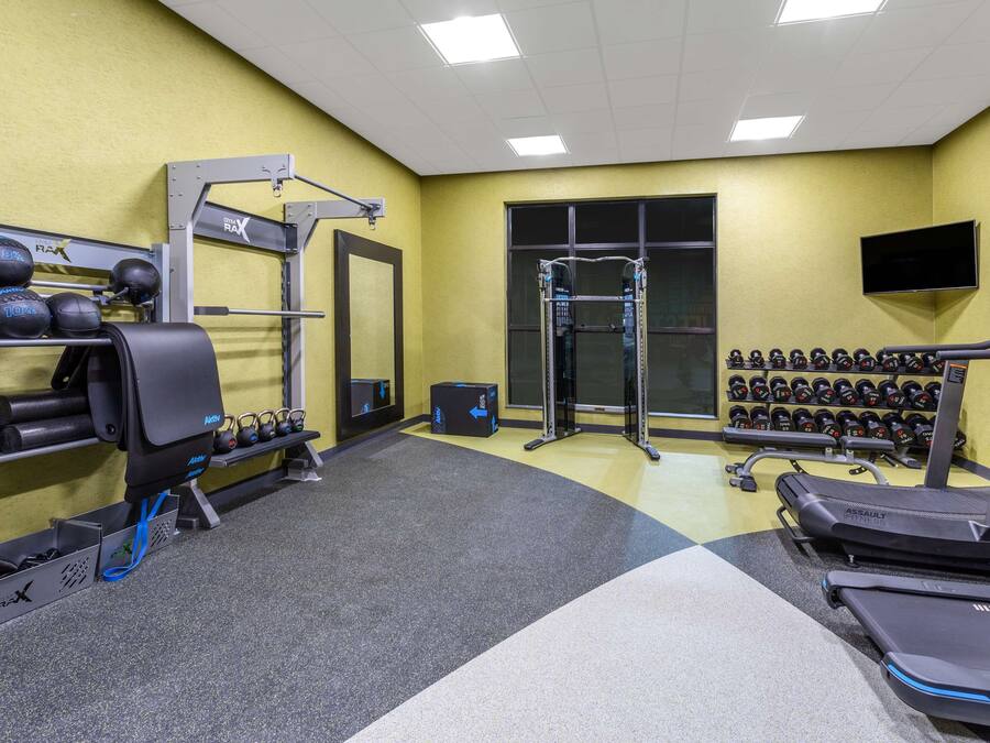 Un gimnasio con equipo de levantamiento de pesas, cintas de correr y un televisor montado en la pared.