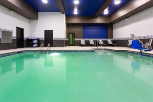 Una piscina interior con agua cristalina, rodeada de sillones de descanso y una puerta que da a otra habitación.