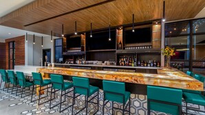 A modern bar area with a marble countertop, green bar stools, and a variety of bottles.