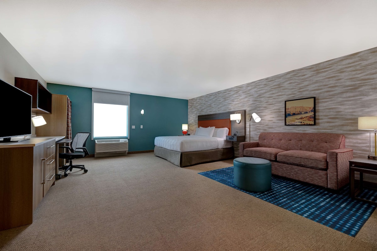 A hotel room with a bed, a desk, a chair, a sofa, a TV, and a window.