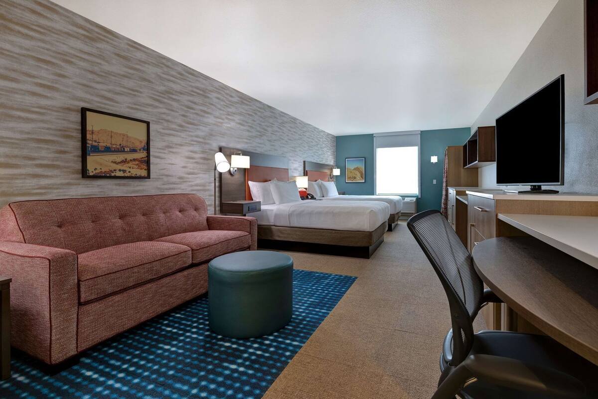 A hotel room with a bed, a sofa, a desk, a television, and a painting on the wall.