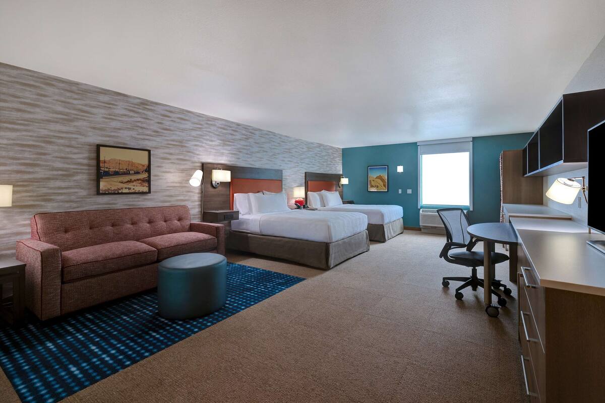 A hotel room with a sofa, two beds, a desk, and a TV.