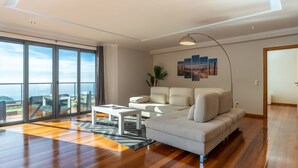 Uma sala de estar ampla com uma grande porta de vidro deslizante que dá para uma varanda, um sofá branco, uma mesa de centro e uma luminária pendente moderna.