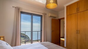Quarto com uma cama grande, um guarda-roupa e vista para o mar através de uma porta de correr.